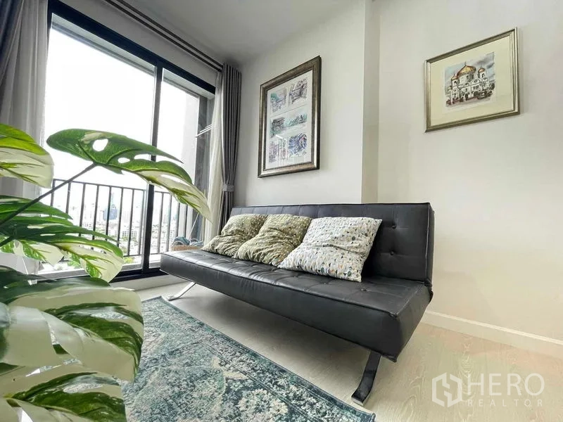 公寓 出售在Huai Khwang, Bangkok - 客厅设黑色沙发与地毯，推拉玻璃门通向可观景的阳台。