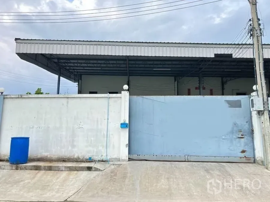 Factory for rent in Samut Prakan - Gated factory entrance with high concrete wall, sliding metal gate and covered loading roof in Bang Phli.