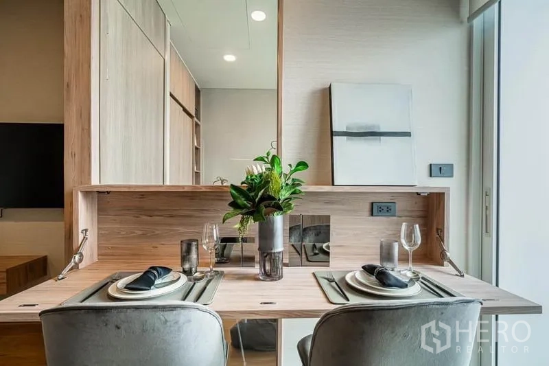 Condominium for sale in Khlong Toei, Bangkok - Compact dining nook for two with a fold-down wooden table, mirror backsplash, and modern place settings.
