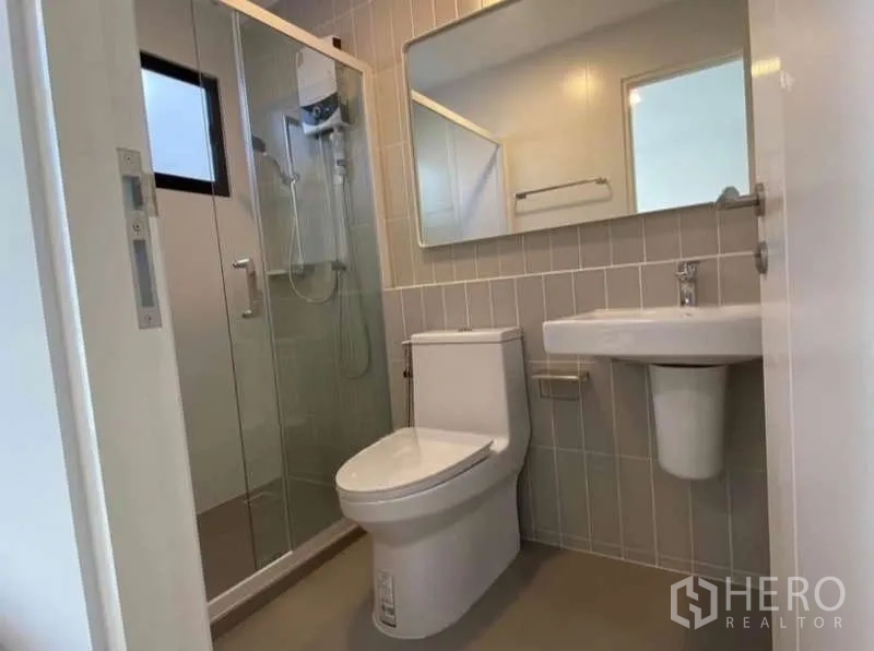 Townhouse for rent in Bang Phli, Samut Prakan - Modern bathroom with glass-enclosed shower, large mirror, toilet and wall tiles.