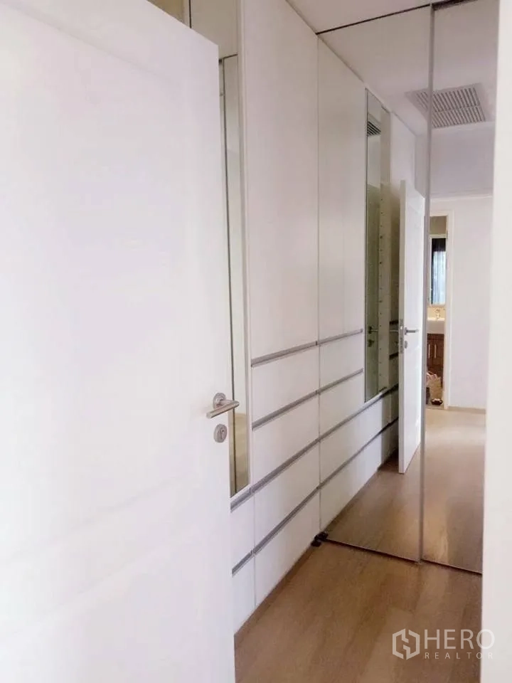 Condominium for rent in Bangkok - Hallway with floor‑to‑ceiling built‑in wardrobes and mirrored doors over wood flooring.