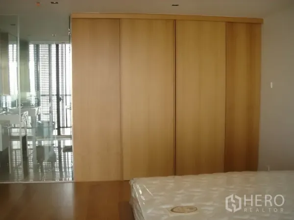 Condominium for rent in Sathon, Bangkok - Master bedroom with large wooden wardrobes and access to a glass-enclosed bathroom.