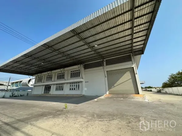 Factory for rent in Samut Prakan - Front view of industrial building with covered loading bay, office windows, and driveway within a walled compound.