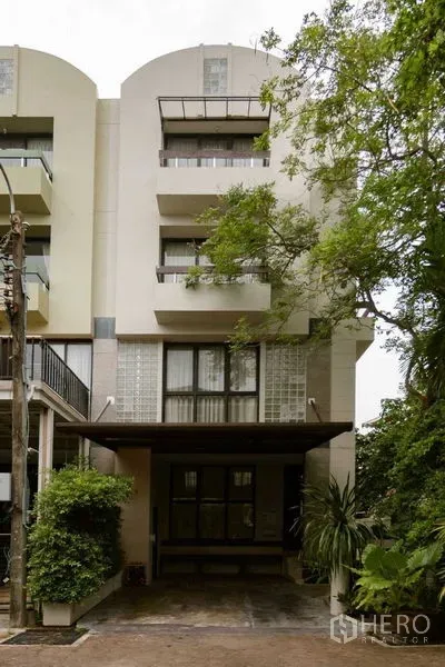 สำนักงานที่บ้าน ขายในWatthana, Bangkok - ด้านหน้าอาคารทาวน์โฮมสมัยใหม่ มีระเบียง โรงจอดรถ และต้นไม้ใหญ่