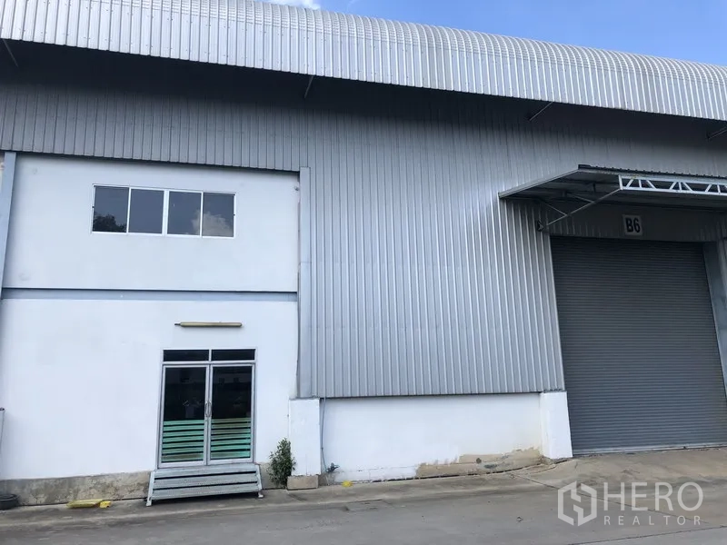 Factory for rent in Khlong Luang, Pathum Thani - Factory exterior with metal cladding, glass entry door and a covered loading bay with roller shutter.