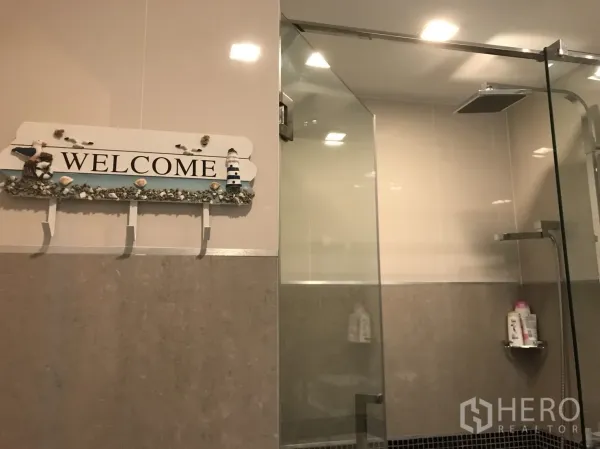 Condominium for rent in Bang Lamung, Chon Buri - Modern bathroom with glass-enclosed rain shower and warm recessed lighting.