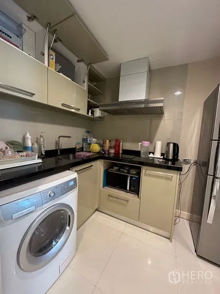 Condominium for rent in Khlong Toei, Bangkok - Compact L-shaped modern kitchen with washing machine, hood, microwave and fridge.