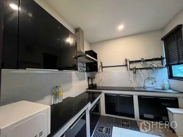 独立式住宅 出租在Mueang Nonthaburi, Nonthaburi - 现代厨房，黑色亮面橱柜、油烟机与转角窗。