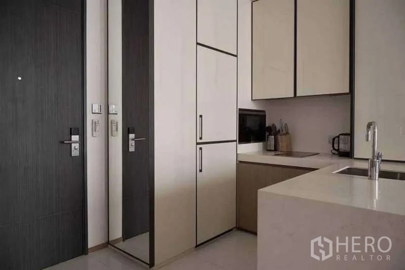 Condominium for rent or sale in Khlong Toei, Bangkok - Compact corner kitchen with integrated appliances and dark entrance door.