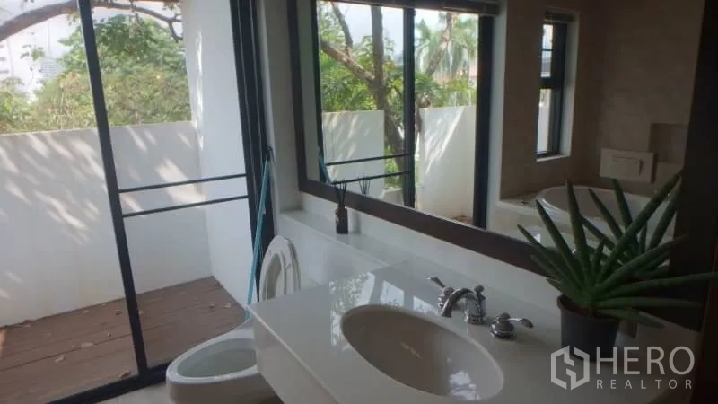 Detached House for rent in Watthana, Bangkok - Bathroom vanity with large mirror and sliding doors opening to a balcony with leafy views.