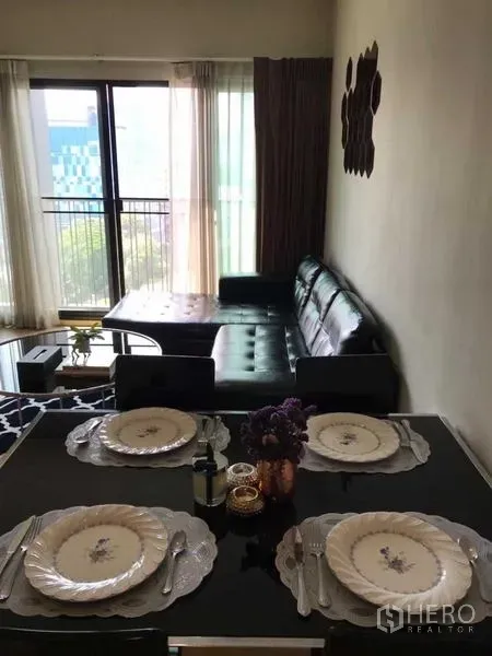 公寓 出租在Watthana, Bangkok - 采光良好的客餐厅，四人餐桌、黑色皮沙发与通往阳台的落地窗