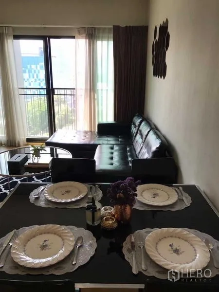 公寓 出租在Watthana, Bangkok - 采光良好的客餐厅，四人餐桌、黑色皮沙发与通往阳台的落地窗