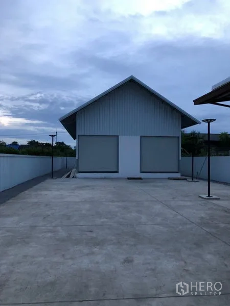 Warehouse for rent in Bueng Kum, Bangkok - Gable-roof warehouse with twin roller shutters and a wide concrete yard at dusk