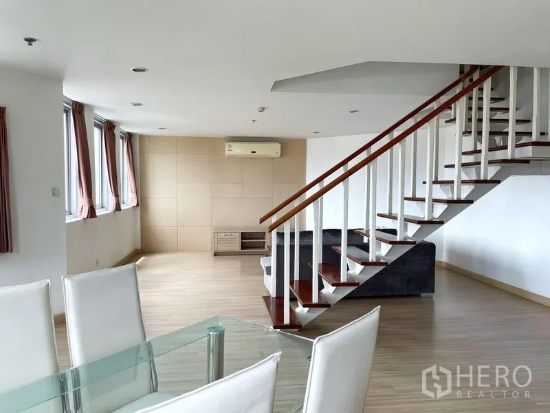 Condominium for rent in Khlong Toei, Bangkok - Living room with a row of windows, staircase and dining table in an open-plan layout.