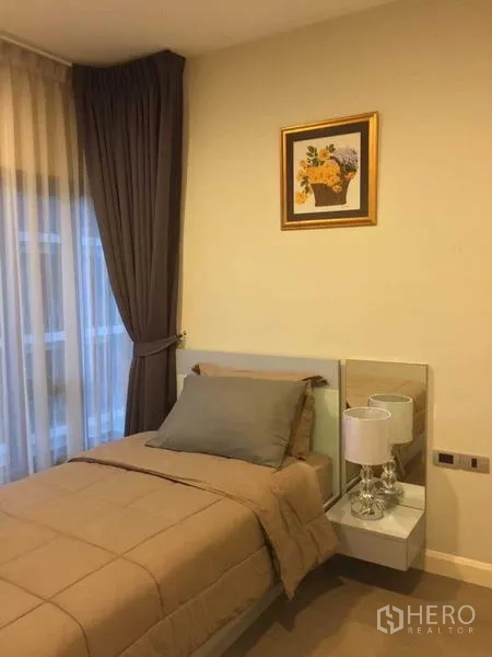 Condominium for rent in Khlong Toei, Bangkok - Second bedroom with a single bed, bedside lamp and floor-to-ceiling curtains.