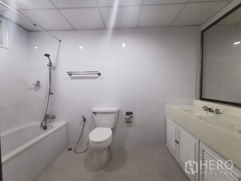 Apartment for rent in Khlong Toei, Bangkok - Bright bathroom with bathtub and shower combo, white vanity and toilet.