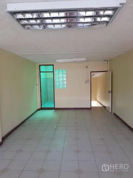 Retail Space for rent in Khlong Toei, Bangkok - Open tiled space with fluorescent lighting and a doorway to a bathroom behind a glass‑block partition.