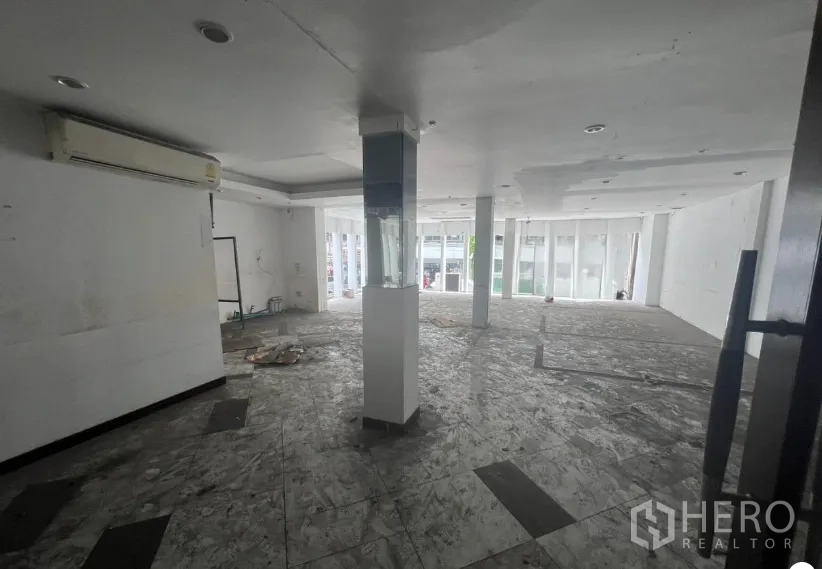 Shophouse for rent in Khlong Toei, Bangkok - Open-plan interior floor with white ceiling, support columns, large front windows and unfinished flooring.