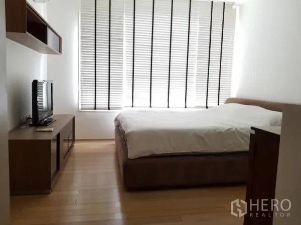 Condominium for rent in Khlong Toei, Bangkok - Bright bedroom with large window blinds, wood floors, queen bed, and TV console.