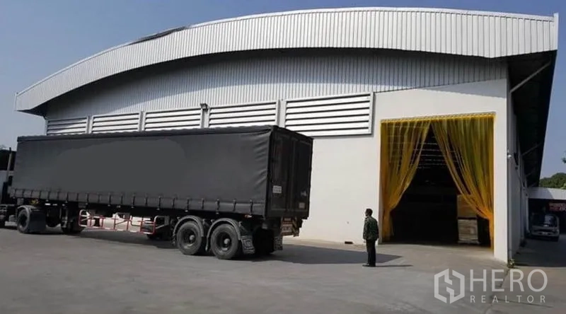 Warehouse for rent or sale - Warehouse exterior with wide driveway and a semi-trailer at the loading bay.