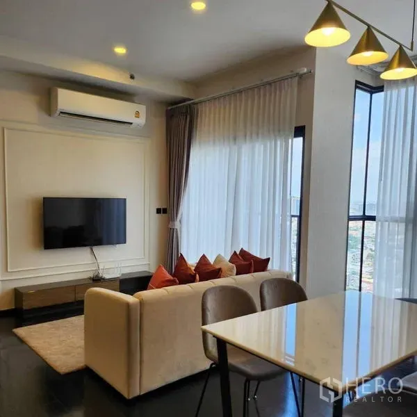 公寓 出租在Watthana, Bangkok - 明亮的客厅，配有沙发、壁挂电视、餐桌与落地窗，俯瞰曼谷景色。