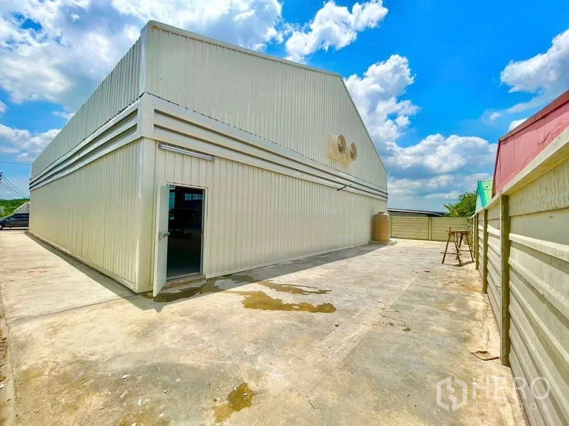 Warehouse for rent in Lam Luk Ka, Pathum Thani - Rear exterior of a white metal-clad warehouse with a wide concrete yard and side door.