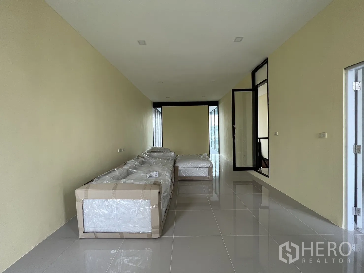 Detached House for rent or sale in Phra Khanong, Bangkok - Alternate angle of the long room with wrapped sofas and tiled floor.