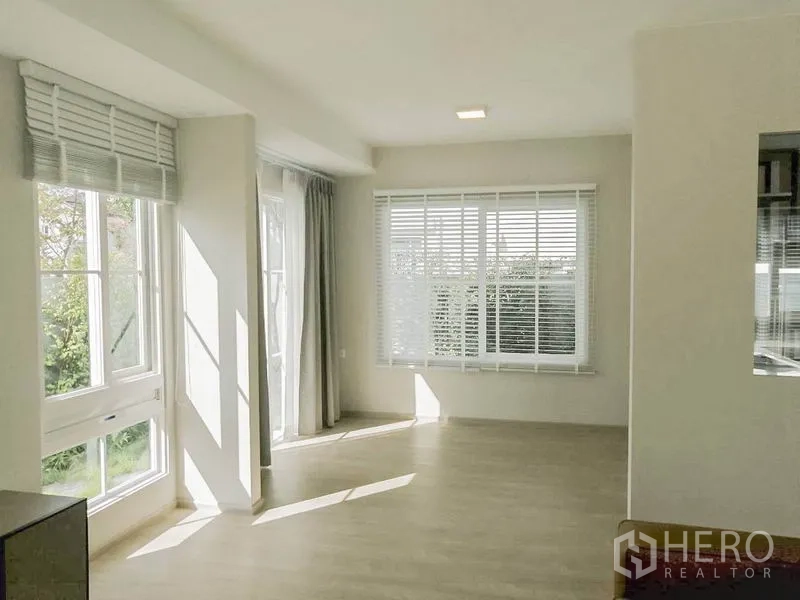 Townhouse for rent in Prawet, Bangkok - Sunlit open-plan living and dining area with multiple windows, blinds and sheer curtains overlooking greenery.