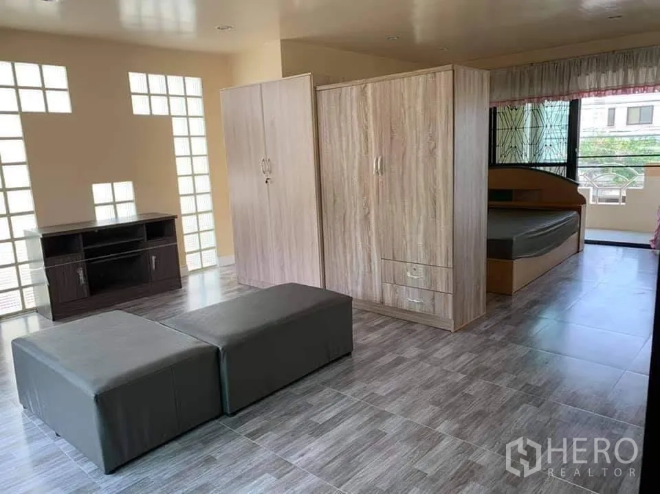 Townhouse for rent in Phra Khanong, Bangkok - Open-plan upper floor with beds, wardrobes, large windows with security grilles, and a glossy ceiling.
