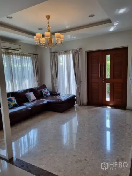 Detached House for rent in Mueang Nonthaburi, Nonthaburi - Spacious living room with chandelier lighting, leather sectional sofa and solid wooden front door.