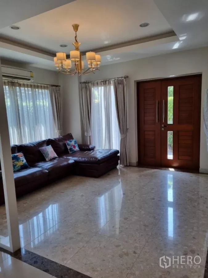 Detached House for rent in Mueang Nonthaburi, Nonthaburi - Spacious living room with chandelier lighting, leather sectional sofa and solid wooden front door.
