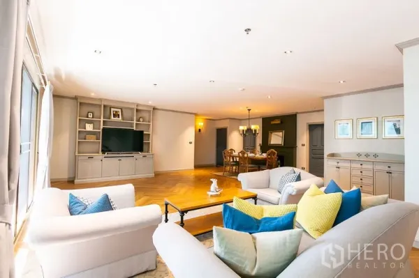 Apartment for rent in Watthana, Bangkok - Spacious open-plan living and dining room with built-in TV wall, colorful cushions and herringbone wood floors.
