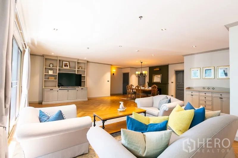 Apartment for rent in Watthana, Bangkok - Spacious open-plan living and dining room with built-in TV wall, colorful cushions and herringbone wood floors.