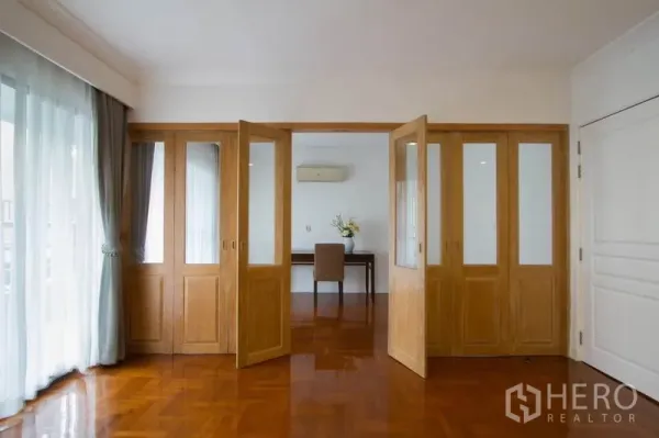 Condominium for rent in Watthana, Bangkok - Glass and wood folding doors opening to a bright study with balcony drapes.