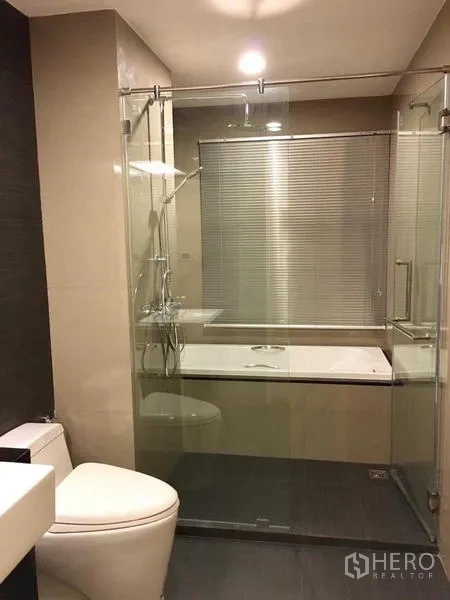 Condominium for rent in Khlong Toei, Bangkok - Modern bathroom with glass-enclosed shower, bathtub and toilet.