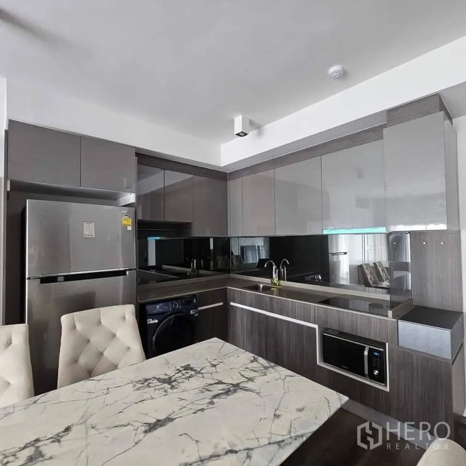 คอนโด for rent in Huai Khwang, Bangkok - ครัวรูปตัวแอลสมัยใหม่พร้อมตู้บานเงา อ่างล้างจาน เตา ไมโครเวฟ และเครื่องซักผ้า