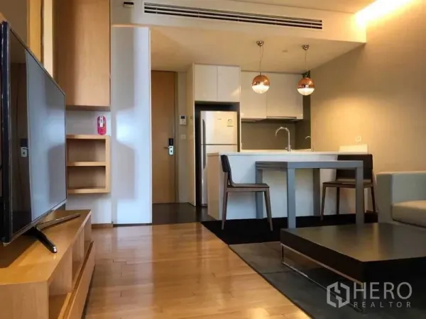 公寓 出租在Watthana, Bangkok - 客厅面向厨房岛台，配电视柜与木地板。
