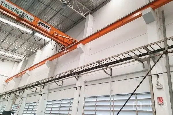 Factory for sale in Rayong - Close-up of overhead crane beam with cable trays and louvered ventilation windows along the wall.