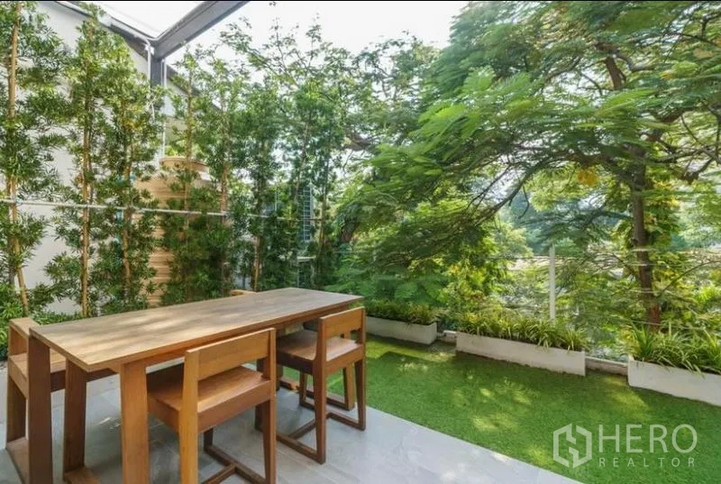 联排别墅 出租在Khlong Toei, Bangkok - 半露天露台，木质餐桌椅、人造草坪与郁郁葱葱的树木