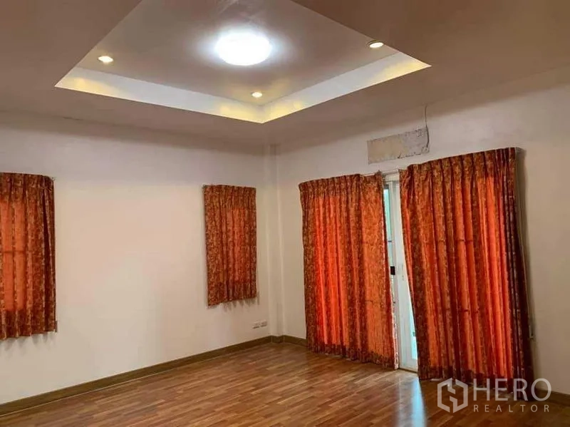 Detached House for sale in Sai Mai, Bangkok - Spacious room with tray ceiling, recessed lights, red curtains and wood floor.