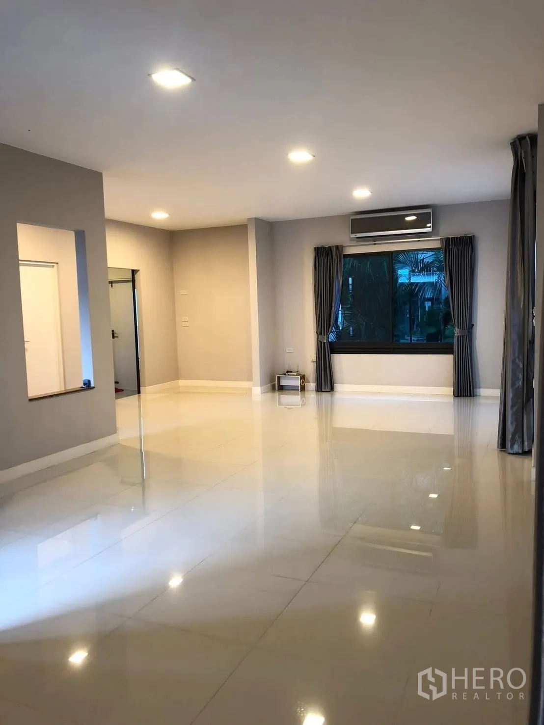 Detached House for rent in Prawet, Bangkok - Open-plan living area with white tiled floor, large window and a wall-mounted air conditioner.