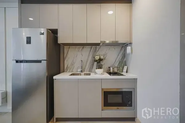 Condominium for sale in Khlong Toei, Bangkok - Compact built-in kitchenette with marble backsplash, cabinets, cooktop, microwave and stainless refrigerator.