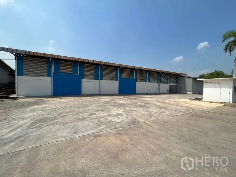Warehouse for rent in Bang Pa-in, Phra Nakhon Si Ayutthaya - Warehouse exterior with blue sliding doors and a large concrete yard for truck maneuvering.