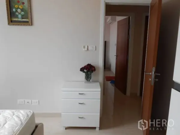 Condominium for rent in Watthana, Bangkok - Bedroom corner with white chest of drawers, wall art, and an open wooden door to the hallway.