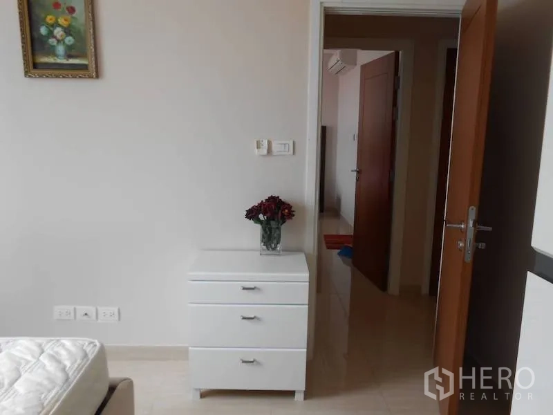 Condominium for rent in Watthana, Bangkok - Bedroom corner with white chest of drawers, wall art, and an open wooden door to the hallway.