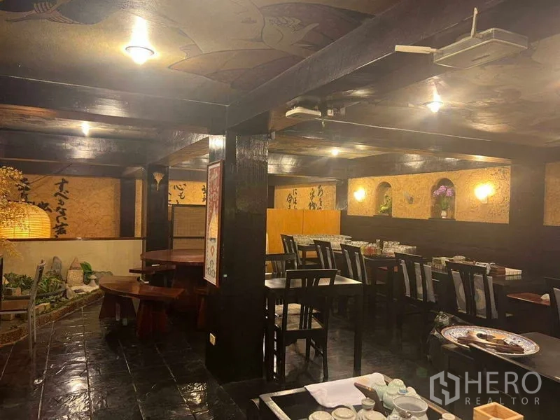 Shophouse for rent in Khlong Toei, Bangkok - Spacious dining area with dark wood beams, multiple tables, and ambient wall lighting.