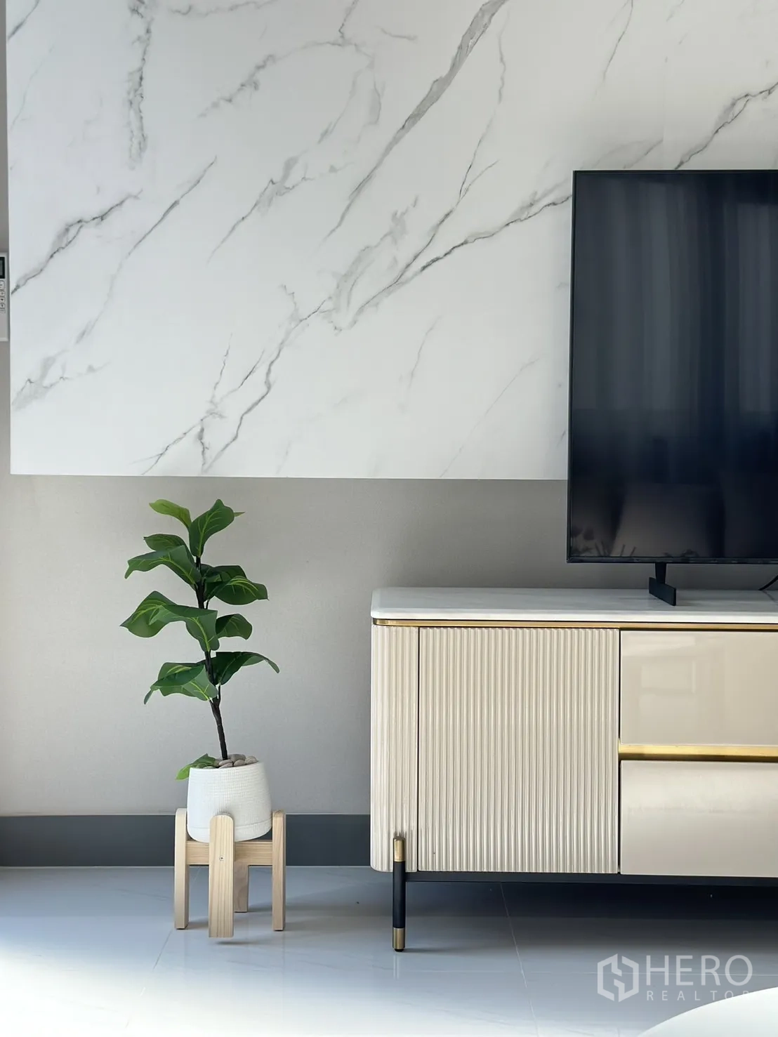 Detached House for rent or sale - TV console detail with marble wall, potted plant on wooden stand and modern cabinet legs.