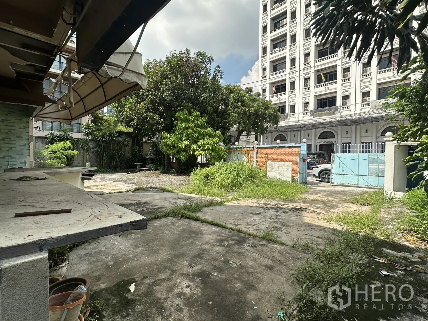 独栋房屋 for rent in Watthana, Bangkok - 侧院带雨篷与水泥露台，蓝色大门通向街道。