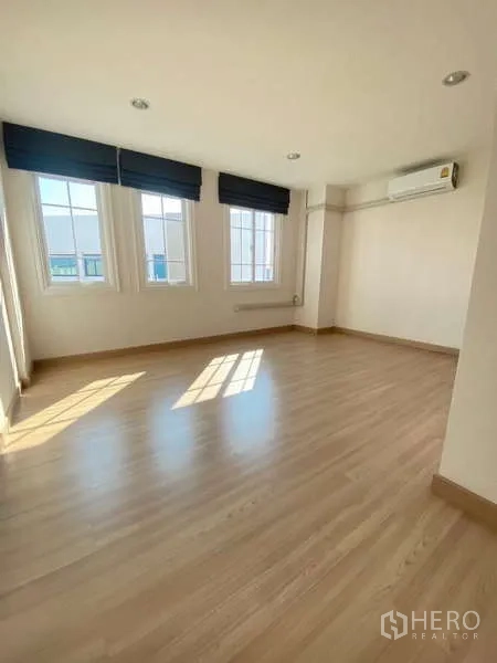 Home Office for rent or sale - Corner bedroom with wood floors, three windows and a wall-mounted air conditioner.