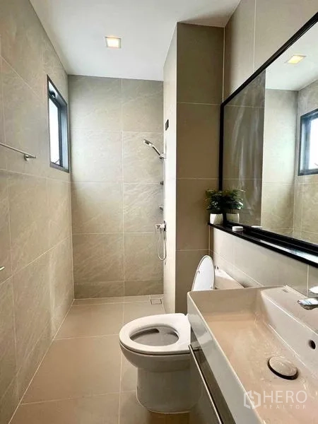 Detached House for rent or sale in Bang Phli, Samut Prakan - Contemporary bathroom with walk-in shower, large mirror, vanity and toilet in neutral tiles.